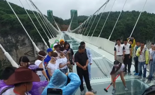 Shouldn’t someone stop this girl? Chinese officials staged a demo of the toughness of “longest, tallest glass bridge.” (Image courtesy of New China TV.)