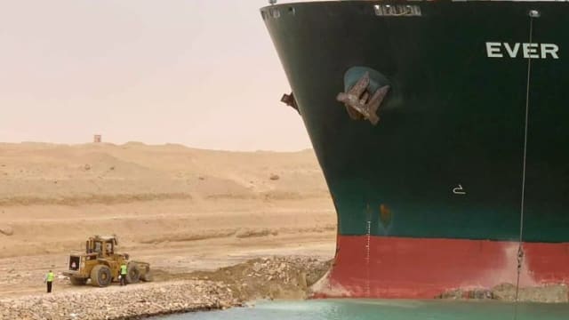 The Ever Given towers over a backhoe trying to dislodge it from the bank of the Suez Canal. (Credit: AP/Suez Canal Authority.)